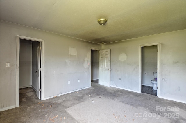 unfurnished bedroom featuring a walk in closet, connected bathroom, and baseboards