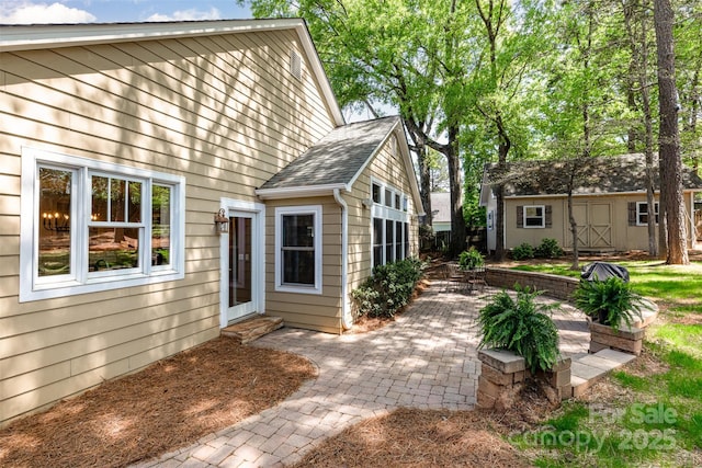 exterior space featuring a patio, an outbuilding, roof with shingles, and a storage shed