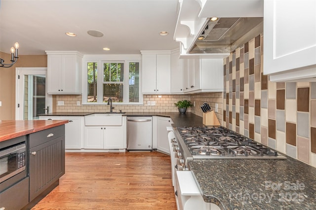 kitchen with wall chimney exhaust hood, a sink, white cabinets, appliances with stainless steel finishes, and recessed lighting