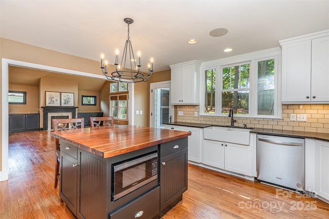 kitchen featuring stainless steel appliances, a sink, butcher block counters, white cabinets, and a fireplace