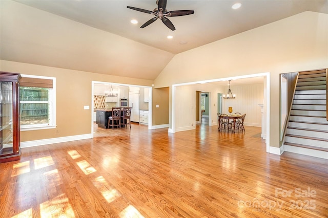 living area with a chandelier, vaulted ceiling, stairs, ceiling fan, and light wood-style flooring