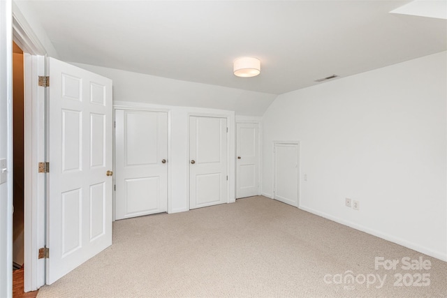 unfurnished bedroom featuring carpet flooring, two closets, vaulted ceiling, and baseboards