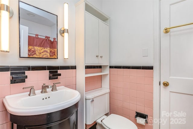 full bathroom featuring tile walls, a sink, toilet, and a wainscoted wall