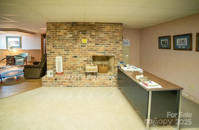 carpeted living area featuring wood walls, a drop ceiling, and wainscoting
