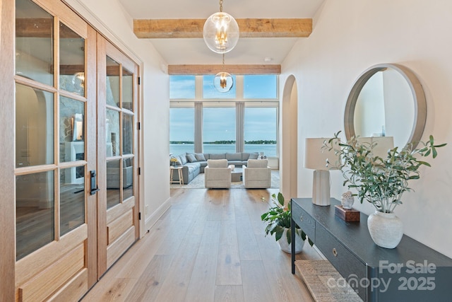 hallway featuring beamed ceiling, a water view, french doors, arched walkways, and light wood finished floors
