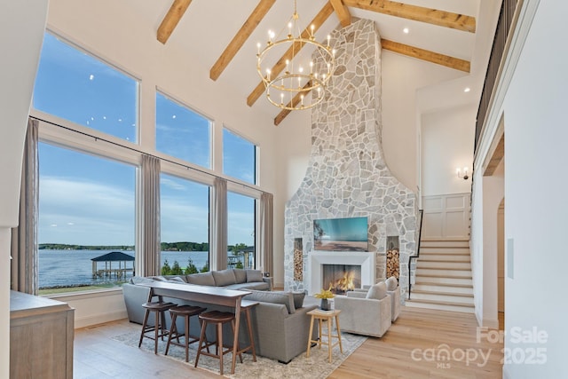 living area featuring a stone fireplace, beam ceiling, high vaulted ceiling, a chandelier, and light wood-style floors
