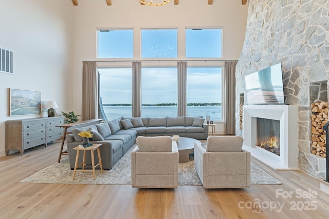 living room with a stone fireplace, a high ceiling, visible vents, and wood finished floors