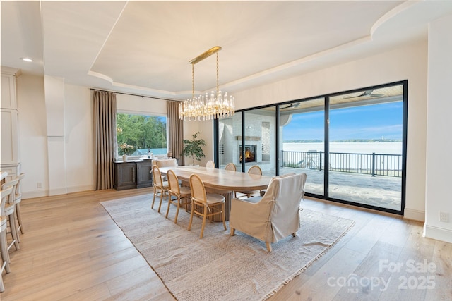 dining room featuring light wood-style floors, a raised ceiling, baseboards, and a notable chandelier