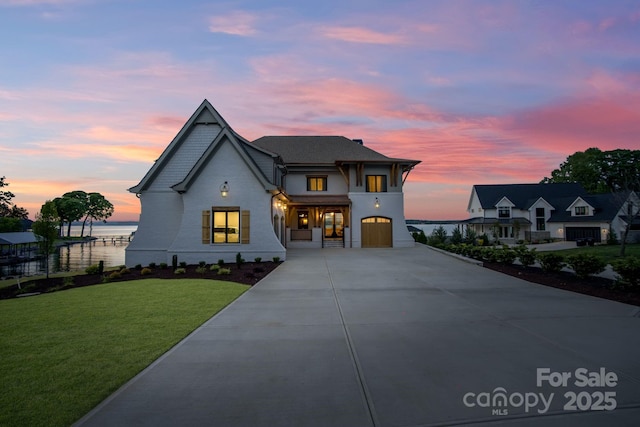 view of front facade with an attached garage, a water view, a front lawn, and concrete driveway
