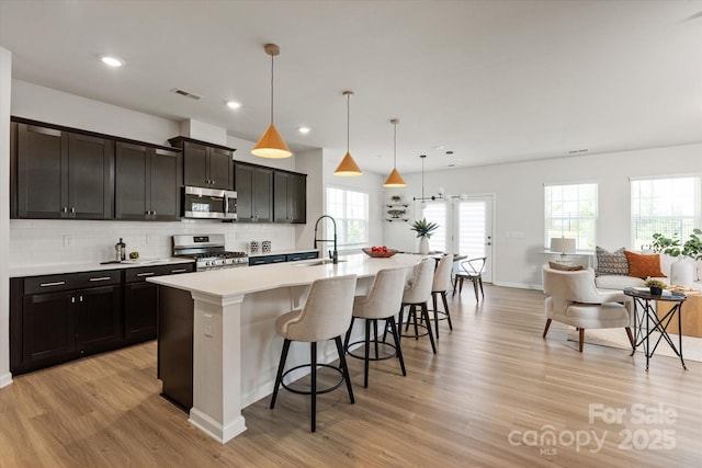 8000 Millbridge Pkwy, Waxhaw, NC 28173 - kitchen featuring appliances with stainless steel finishes, a sink, light wood-style flooring, a center island with sink, and a kitchen bar
