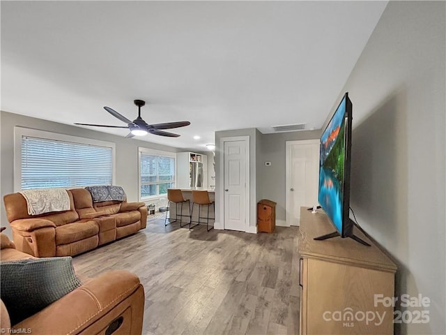 living room with baseboards, a ceiling fan, light wood-style floors, and visible vents