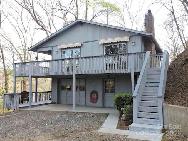 view of front of house featuring stairway, dirt driveway, a chimney, a garage, and a deck