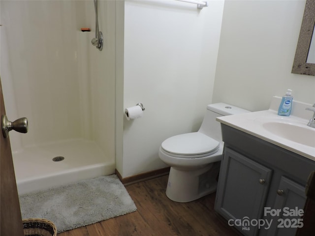 full bath with toilet, vanity, wood finished floors, and a stall shower