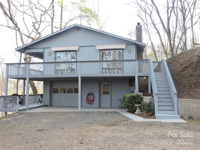 view of front of home featuring a chimney, driveway, an attached garage, stucco siding, and stairs