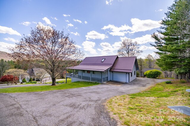 farmhouse inspired home with a front lawn, an attached garage, driveway, a porch, and metal roof