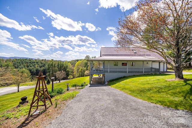 farmhouse with a front lawn, driveway, a porch, metal roof, and a forest view