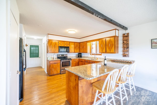 kitchen with a peninsula, brown cabinetry, a sink, and black appliances