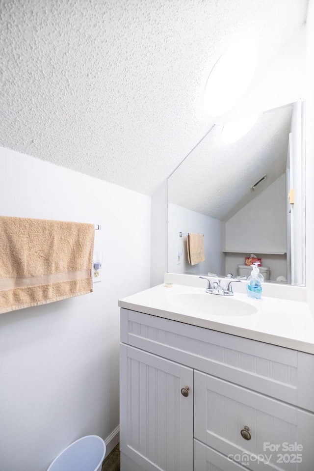 bathroom featuring lofted ceiling, vanity, a textured ceiling, and visible vents