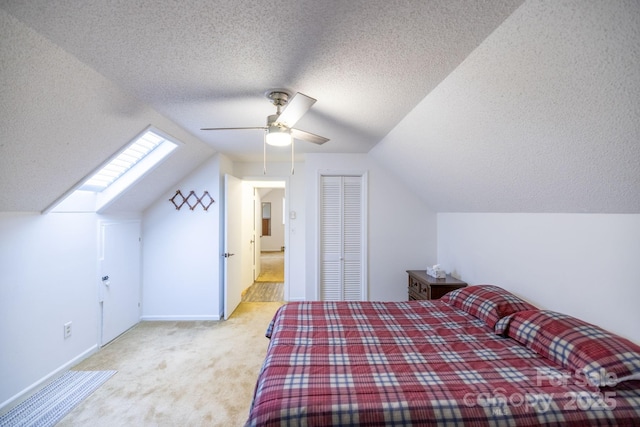 carpeted bedroom featuring ceiling fan, lofted ceiling with skylight, a textured ceiling, and a closet