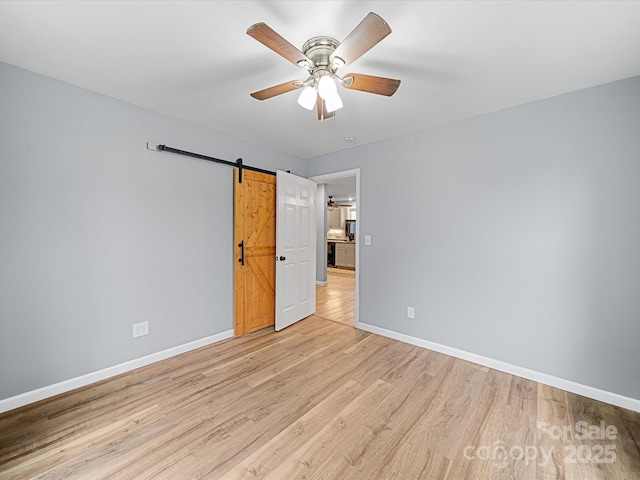 unfurnished bedroom featuring baseboards, light wood-type flooring, a ceiling fan, and a barn door