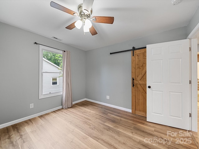 spare room featuring a barn door, light wood-style flooring, baseboards, and a ceiling fan