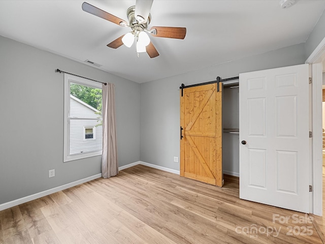 unfurnished bedroom with light wood-style floors, baseboards, a barn door, and ceiling fan