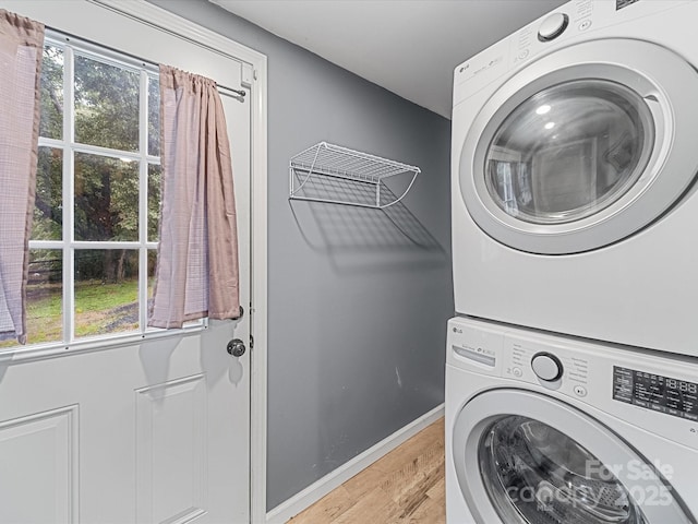 washroom featuring stacked washer and clothes dryer, light wood-style flooring, and baseboards