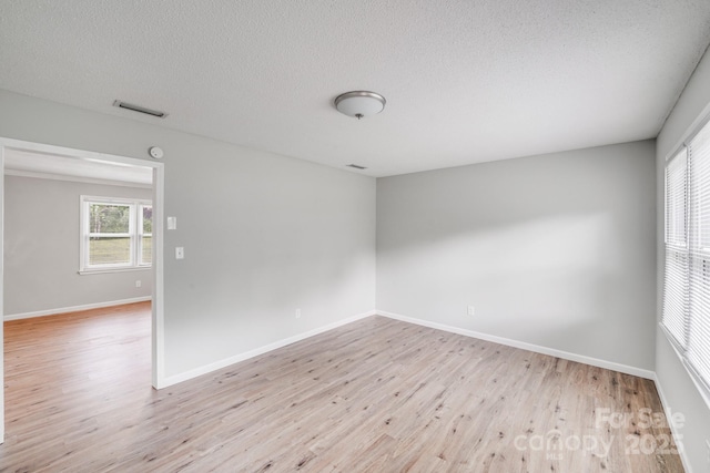 empty room featuring light wood-style floors, baseboards, visible vents, and a textured ceiling