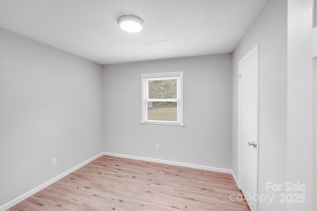 spare room featuring light wood-type flooring, baseboards, and a textured ceiling
