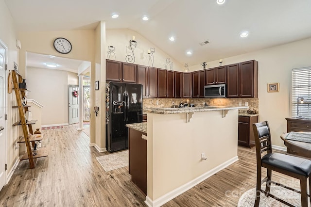 3939 Archer Notch Ln, Huntersville, NC 28078 - kitchen with stainless steel microwave, black fridge, a breakfast bar area, dark brown cabinets, and decorative backsplash