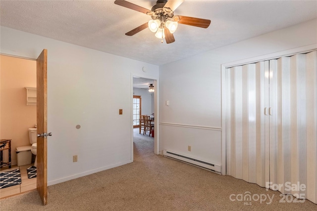 unfurnished bedroom with a baseboard radiator, light colored carpet, baseboards, a ceiling fan, and ensuite bathroom