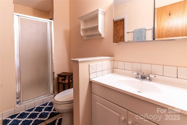 bathroom featuring a stall shower, toilet, vanity, and backsplash
