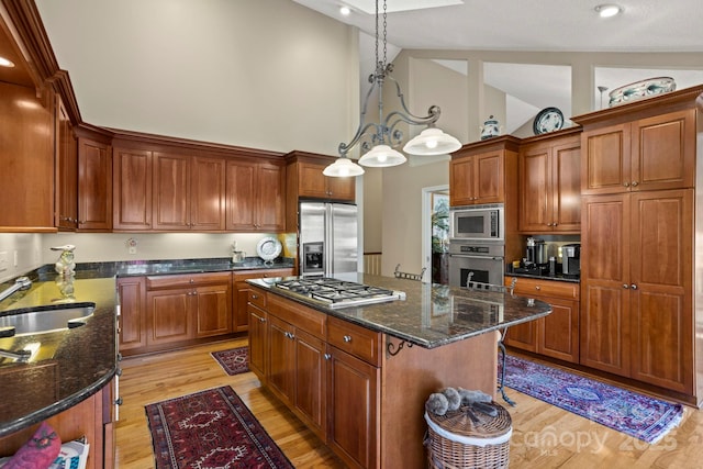 kitchen featuring stainless steel appliances, a center island, light wood finished floors, a sink, and high vaulted ceiling
