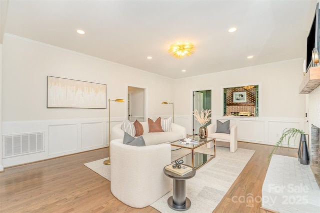 426 Walden Trl, Waxhaw, NC 28173 - living room with visible vents, a fireplace, wainscoting, a decorative wall, and light wood-style flooring