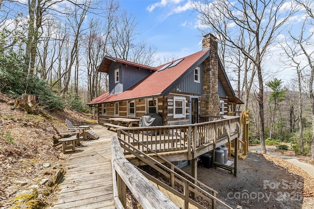 rear view of house with a wooden deck, a shingled roof, a chimney, and log siding