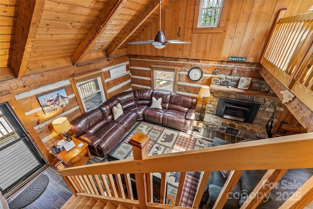 living area featuring lofted ceiling with beams, a stone fireplace, wood walls, and wood ceiling