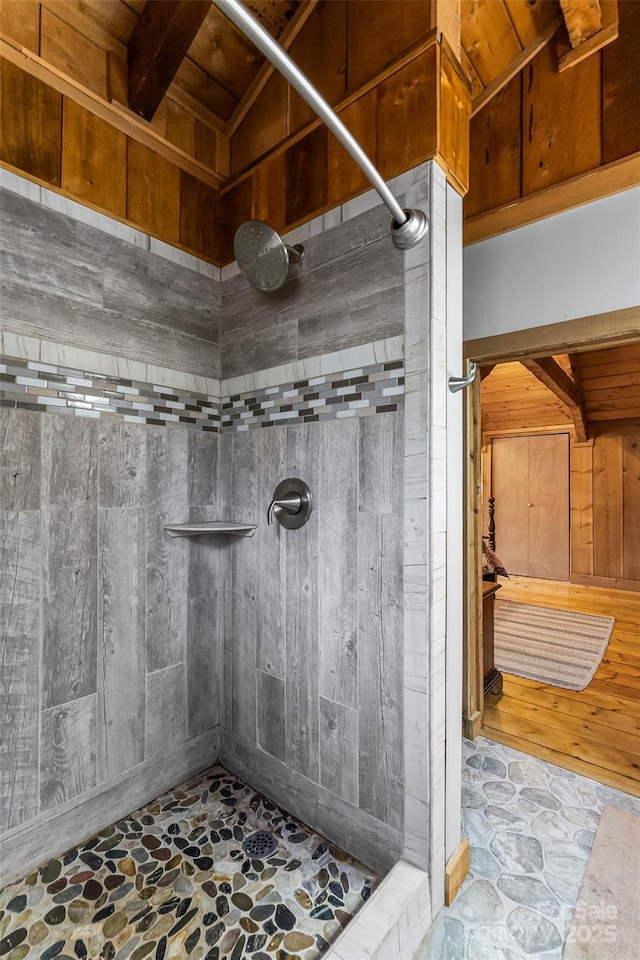 bathroom with wood ceiling, wood walls, stone flooring, and a tile shower