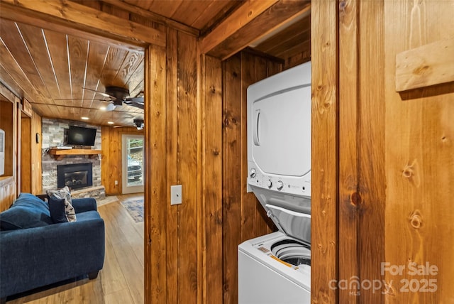 washroom featuring a ceiling fan, a fireplace, wood ceiling, wooden walls, and stacked washing maching and dryer
