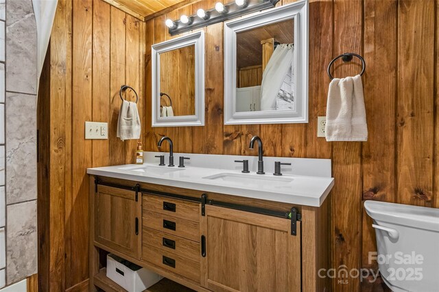 full bathroom featuring wooden walls, a sink, double vanity, and toilet