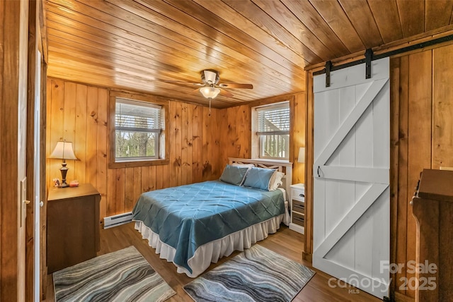 bedroom featuring a barn door, a baseboard radiator, wood finished floors, wooden walls, and wood ceiling