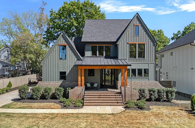 modern inspired farmhouse featuring brick siding, fence, board and batten siding, and covered porch