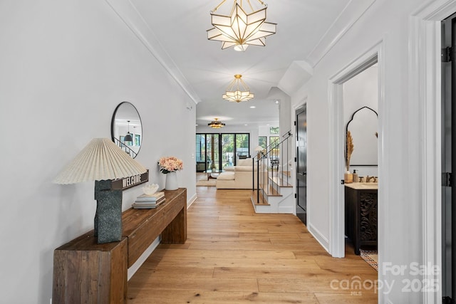 corridor featuring stairs, ornamental molding, a chandelier, and light wood-style floors