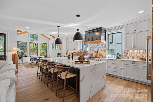 kitchen featuring recessed lighting, light stone counters, backsplash, open floor plan, and custom range hood