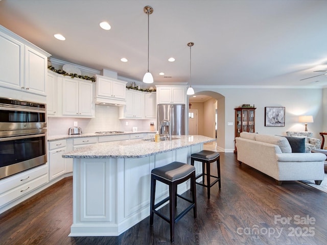 kitchen with arched walkways, a sink, dark wood-style flooring, open floor plan, and appliances with stainless steel finishes