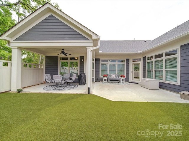 rear view of property with a patio area, a ceiling fan, fence, a yard, and roof with shingles