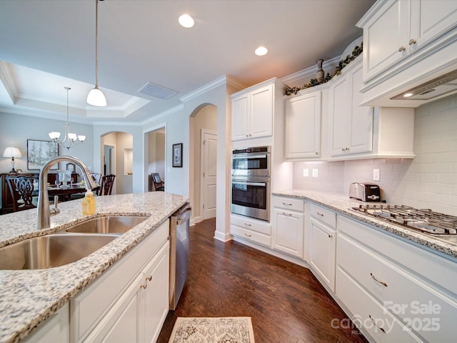 kitchen featuring tasteful backsplash, a sink, arched walkways, stainless steel appliances, and ornamental molding