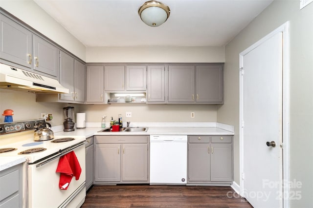 kitchen featuring dark wood finished floors, under cabinet range hood, a sink, white appliances, and gray cabinetry