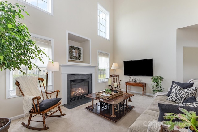 carpeted living room with plenty of natural light, a high ceiling, and a fireplace with flush hearth