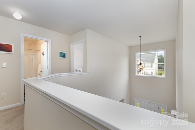 hall with baseboards, light carpet, an upstairs landing, and a chandelier