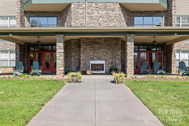 entrance to property featuring an outdoor stone fireplace, french doors, and a lawn